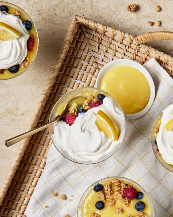 Curd au citron - parfait Un plat en verre de parfait au citron est présenté sur un plateau en osier avec un bol de lemon curd et trois autres parfaits.