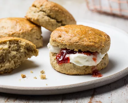 Une assiette de scones, dont un garni de crème caillée et de confiture