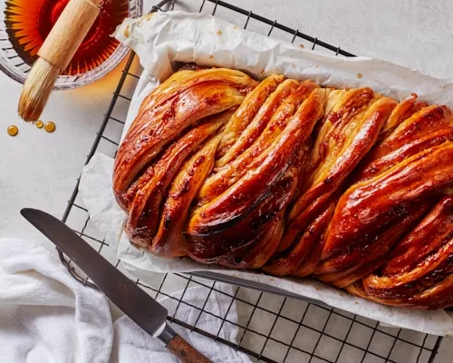 Babka aux pommes épicées dans un plat à four sur une grille de refroidissement avec un bol de sirop de miel et de cassonade.